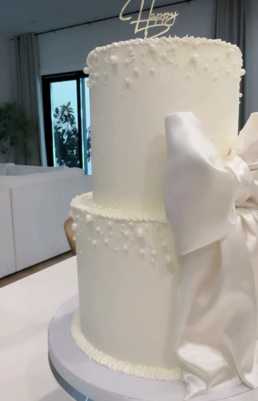 Two-tier white cake with a satin bow and pearl dots