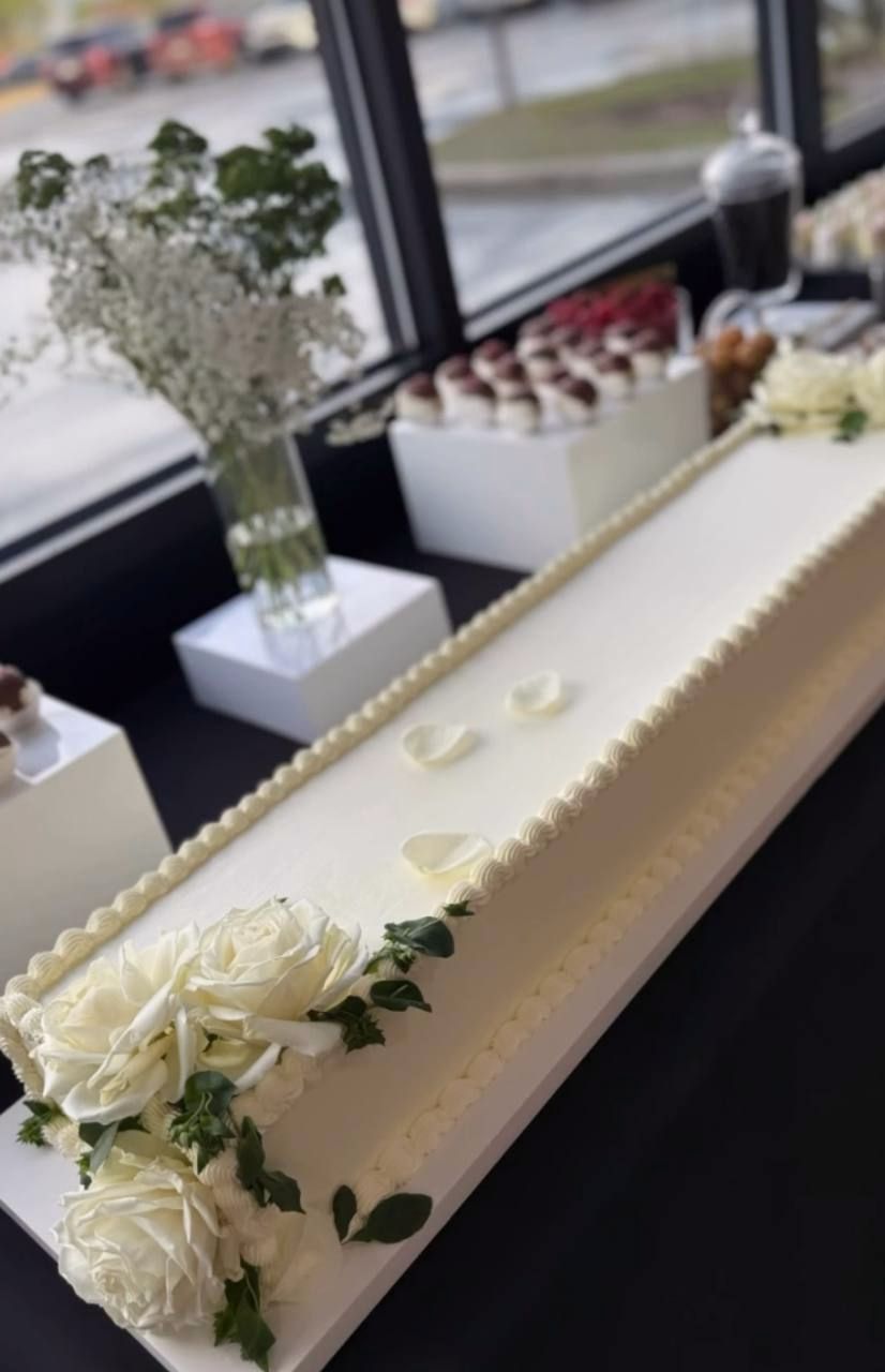 Long white celebration cake with white roses on a dessert table